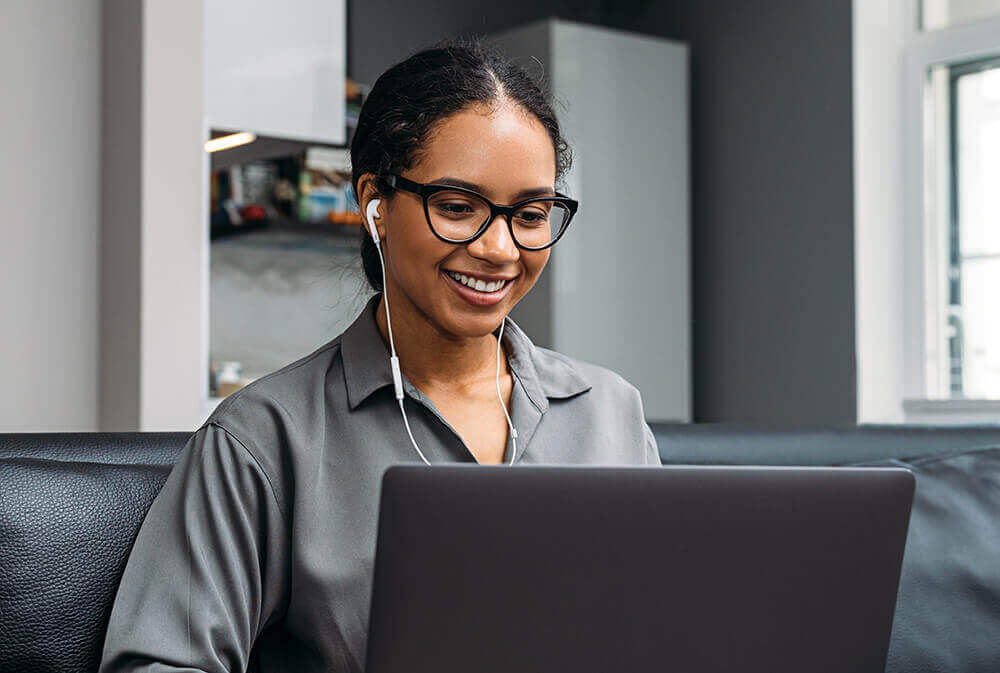 women in glasses wearing headphones and smiling at a laptop